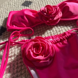 Detailed view of 3D satin rose flower on rose red bandeau bikini on a knit rug background