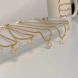 Détail de colliers dorés avec pendentifs lettres sertis de zircons sur plateau en verre