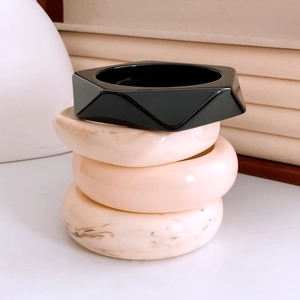 Détail de bracelets empilés en acrylique noir géométrique et motif marbre crème
