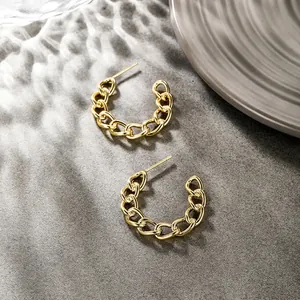 Detailed close-up of golden Cuban link C-shape earrings on a textured grey background