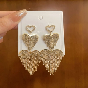 Macro shot of gold three-heart tassel earrings with shiny rhinestones on a white card