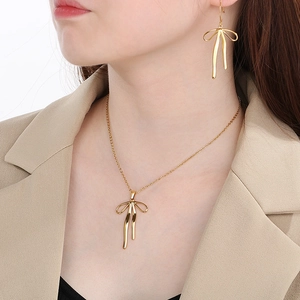 Close-up of golden bow-shaped necklace and matching earrings worn by a model