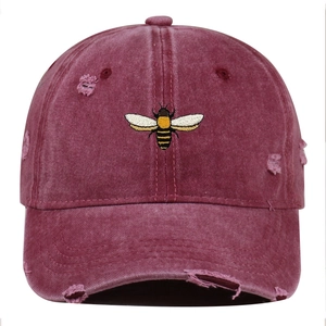 Close-up of bee embroidery and distressed rip details on a washed burgundy baseball cap