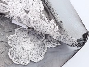 Gros plan sur tissu en maille noire avec broderie florale 3D blanche et dentelle