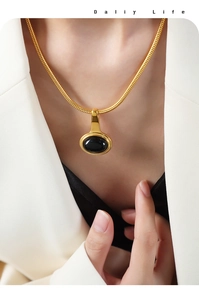 Detail of gold-plated snake chain necklace with black oval pendant worn on a model
