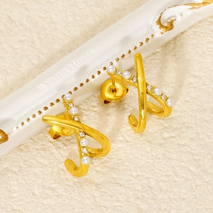 Close-up of gold X-shaped earrings with pearls and crystals on a white frame