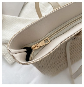 Detail of a smooth golden zipper on a beige straw tote bag with premium leather piping