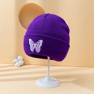 Purple knitted beanie with white butterfly embroidery on a display stand with cotton decor