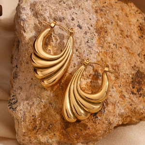 Detailed view of 18K gold plated earrings with fan-shaped wave textures on stone background