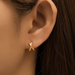 Close-up of golden X-shaped double-row earrings with turquoise inlay worn by a model