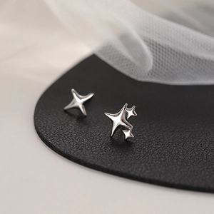 Asymmetric silver four-pointed star stud earrings on a premium black leather texture