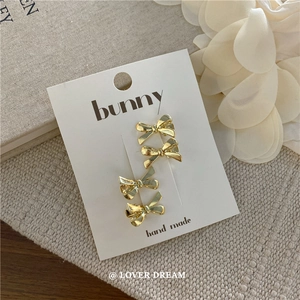 Detail of four gold bow-shaped metal hair clips on a white bunny brand handmade card