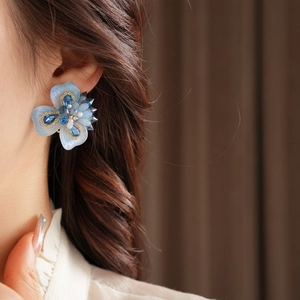 Détail macro de boucles d'oreilles fleur papillon avec cristal bleu et perle sur modèle