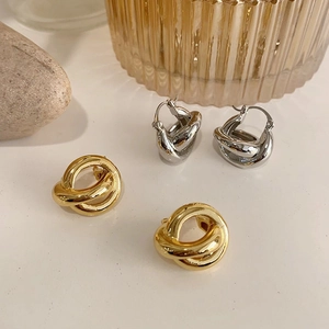 Detail of interlocking knot earrings in gold and silver finish on a minimalist background