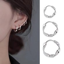 Macro detail of silver twisted wave hoop earrings worn on earlobe and cartilage