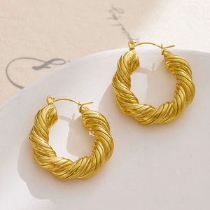 Close-up of golden hoop earrings with twisted rope texture on a white ceramic plate