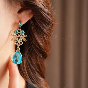 Close-up of vintage gold earrings with blue drop stones and zircon on a model