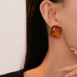 Close-up of square amber resin earring with gold frame worn by a model
