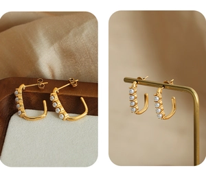 Detail view of U-shaped gold earrings with vertical pearl inlay on a wooden display