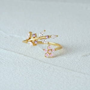 Close-up of golden leaf ring with marquise zircon and pink floral design on textured surface
