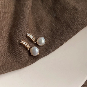 Macro view of Baroque pearl earrings with baguette-cut crystals on brown linen texture
