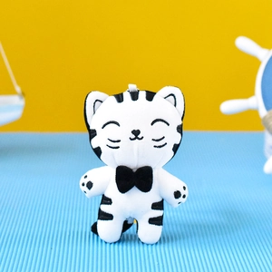 Detail shot of a cute white and black striped plush cat keychain with a black bow