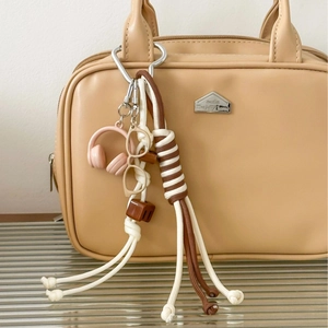 Khaki headphone and glasses charm on a beige leather handbag with braided rope detail