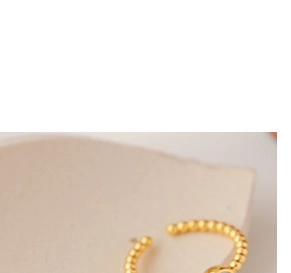 Detail of gold beaded open ring on a ceramic tray showing minimalist metal texture