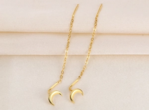 Detail of golden moon and star tassel ear threaders on textured beige fabric
