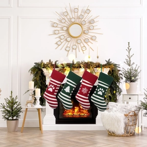 Set of 4 knitted Christmas stockings with paw and snowflake patterns on a cozy fireplace