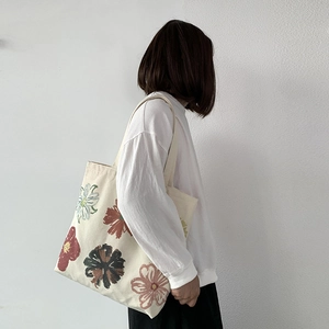 Close-up of beige canvas tote bag with abstract floral prints worn over the shoulder