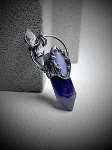 Macro detail of antique silver dragon claw pendant with purple crystal and leaf motif