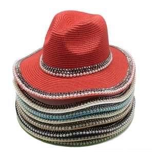 Close-up of colorful stacked straw hats with elegant pearl and silver stud hatbands
