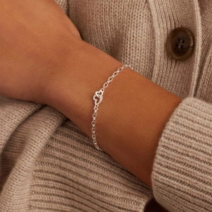 Silver interlocking heart paperclip bracelet on wrist with a beige knit sweater background