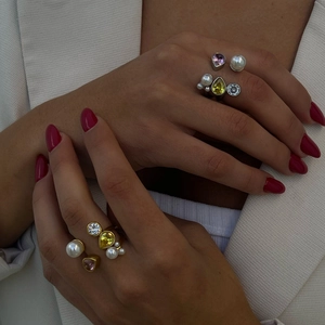 Detailed view of layered stainless steel rings with colorful zircons and pearls on hand