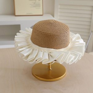 Detail of summer straw hat with oversized white satin ruffled brim on a metal stand