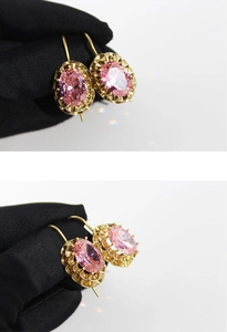 Detail view of retro gold earrings with a pink oval gemstone on a white background