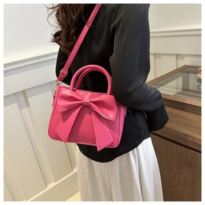 Detail of pink crossbody bag with large decorative bow on model in home setting