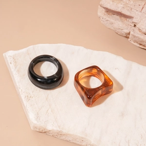 Detail of a minimalist black round acrylic ring and amber square ring on a stone base