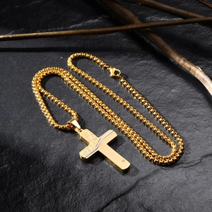Detail of gold cross pendant with cracked texture and small diamond on black slate