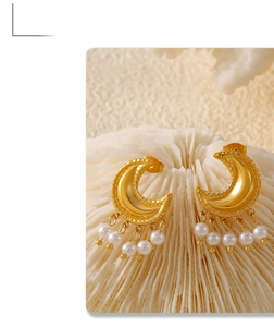 Detail of gold crescent moon tassel earrings with white pearl beads on coral texture