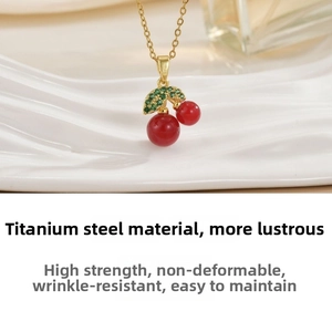 Macro detail of red cherry pendant necklace in gold titanium steel with green zircons