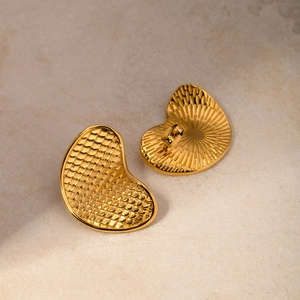 Detail of 18k gold fish-scale textured earrings on beige stone surface in soft lighting
