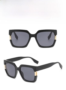 Detail view of square black sunglasses with gold metal hinges and grey lenses