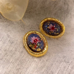 Close-up of vintage oval gold earrings with blue resin, pink dried flowers and pearls