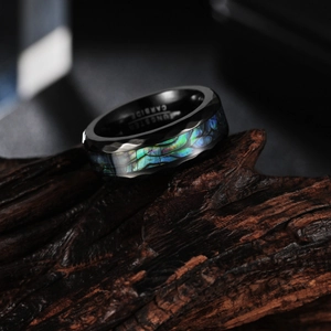 Men's black tungsten carbide ring with abalone shell inlay and faceted edges on wood
