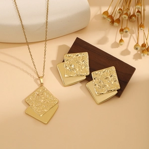 Detailed shot of golden layered square pendant necklace and stud earrings on stone