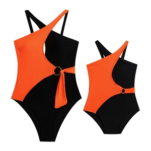 Detail of one-shoulder color-block swimsuit with metal ring and orange ribbons