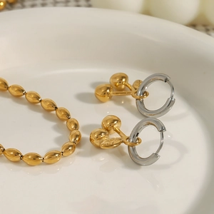 Detail of silver cherry earrings and gold beaded bracelet on a white ceramic plate