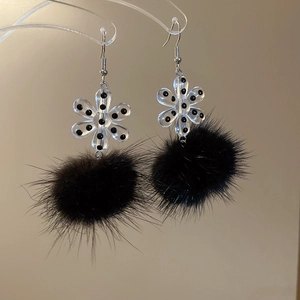Detail of snowflake acrylic flower earrings with black plush pom-poms hanging on a stand